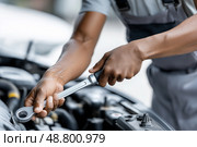 Dedicated Male Mechanic Tightening Engine Bolts, Focused Expression in Garage Workshop. Мужчина-механик затягивает болты двигателя, сосредоточенно работает в гаражной мастерской. Стоковое AI-изображение, AI-художник Katsiaryna Repich / Фотобанк Лори