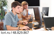 Focused young guy studying in computer lab with fellow students engrossed in coursework. Стоковое видео, видеограф Яков Филимонов / Фотобанк Лори