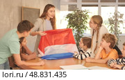 Smiling young female teacher conducting lesson for tweens, showing state flag of Netherlands in audience of middle school. Стоковое видео, видеограф Яков Филимонов / Фотобанк Лори