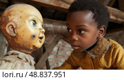 A young boy looks intently at a vintage porcelain doll in an attic setting. The boys facial expression suggests a mix of curiosity and trepidation as he observes the dolls antique features. Стоковое AI-изображение, AI-художник Данила Большаков / Фотобанк Лори