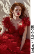 A redheaded woman in a red dress poses under a tree, her flowing hair framing her face. The dress is soft and has a deep V-neck. She wears red lipstick, eyes closed, looking down. Стоковое AI-изображение, AI-художник Данила Большаков / Фотобанк Лори