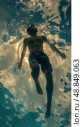 A man swims underwater in a pool with his arms outstretched. The sunlight shines through the water, creating a shimmery effect. Стоковое AI-изображение, AI-художник Данила Большаков / Фотобанк Лори