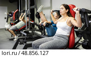 Woman is engaged in sports sitting on simulator in the gym. Woman strengthens muscles of hands on simulator. Стоковое фото, фотограф Яков Филимонов / Фотобанк Лори