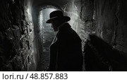 A man wearing a fedora walks through a dark stone tunnel. The image is in black and white and the man is partially obscured by shadows. Стоковое AI-изображение, AI-художник Данила Большаков / Фотобанк Лори