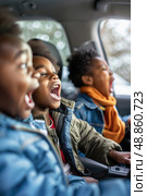 Three young boys sit in the backseat of a car, mouths agape in excitement as they look out the window. Стоковое AI-изображение, AI-художник Данила Большаков / Фотобанк Лори