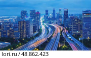 Time-lapse showcases a vast urban landscape at twilight with intricate highway interchanges with streaks of light from vehicles, surrounded by towering modern skyscrapers. Стоковое AI-видео, аниматор Елена Никишина / Фотобанк Лори