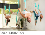 Young European woman doing exercise in hammock in antigravity yoga studio. Female group workout for health. Стоковое фото, фотограф Яков Филимонов / Фотобанк Лори