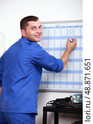 Man filling in wall schedule. Стоковое фото, агентство Ingram Publishing / Фотобанк Лори