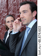 Businessman on a call whilst being watched by a colleague. Стоковое фото, агентство Ingram Publishing / Фотобанк Лори