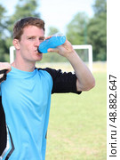 Man stood by soccer pitch drinking energy drink. Стоковое фото, агентство Ingram Publishing / Фотобанк Лори