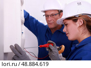 a young woman working on an electricity meter accompanied with a 45 years old man, both are wearing blue jumpsuites. Стоковое фото, агентство Ingram Publishing / Фотобанк Лори