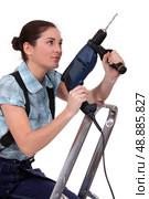 Woman holding drill whilst climbing ladder. Стоковое фото, агентство Ingram Publishing / Фотобанк Лори