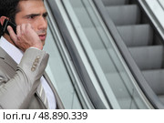 Perturbed businessman using a cellphone by an escalator. Стоковое фото, агентство Ingram Publishing / Фотобанк Лори