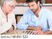 Senior woman and young man playing checkers. Стоковое фото, агентство Ingram Publishing / Фотобанк Лори