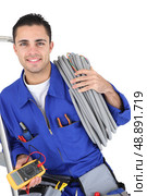 Worker carrying cabling coiled around his shoulder. Стоковое фото, агентство Ingram Publishing / Фотобанк Лори