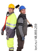Tradesmen standing back to back and holding tools. Стоковое фото, агентство Ingram Publishing / Фотобанк Лори