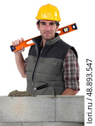 Stonemason standing before a wall and carrying a spirit level. Стоковое фото, агентство Ingram Publishing / Фотобанк Лори