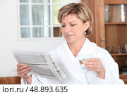 Woman in a bathrobe reading a newspaper and drinking a glass of water. Стоковое фото, агентство Ingram Publishing / Фотобанк Лори