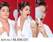 brunette wearing bathrobe with hair curlers holding hairbrush holding  against red background. Стоковое фото, агентство Ingram Publishing / Фотобанк Лори