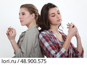 Girl lighting a cigarette as another snaps one in half. Стоковое фото, агентство Ingram Publishing / Фотобанк Лори
