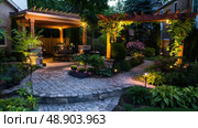 A patio featuring a stone walkway leading to a pergola-covered seating area, surrounded by green plants and flowers. Стоковое AI-изображение, AI-художник Данила Большаков / Фотобанк Лори