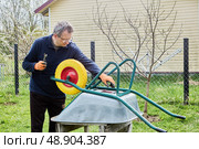 Gardener installing flat free wheel on garden cart to enhance durability and prevent punctures during outdoor tasks. Стоковое фото, фотограф Владимир Григорьев / Фотобанк Лори