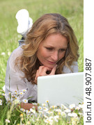 Relaxed woman lying in a field of daisies using her laptop. Стоковое фото, агентство Ingram Publishing / Фотобанк Лори