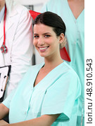 beaming brunette nurse sitting at desk with standing colleagues in background. Стоковое фото, агентство Ingram Publishing / Фотобанк Лори