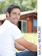 Young man sitting in front of chalet. Стоковое фото, агентство Ingram Publishing / Фотобанк Лори