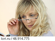 Young woman peering over her glasses at a magazine. Стоковое фото, агентство Ingram Publishing / Фотобанк Лори