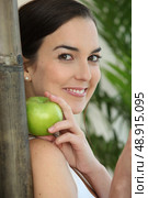 a brunette woman with an apple leaning against a bamboo stick. Стоковое фото, агентство Ingram Publishing / Фотобанк Лори