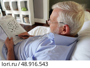 Grey-haired man completing crossword puzzle. Стоковое фото, агентство Ingram Publishing / Фотобанк Лори