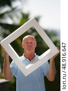 Bald man stood in his garden holding modern art. Стоковое фото, агентство Ingram Publishing / Фотобанк Лори