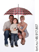Young family sheltering under an umbrella. Стоковое фото, агентство Ingram Publishing / Фотобанк Лори