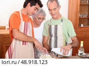 a 20 years old boy and 65 years old man and woman making cake together. Стоковое фото, агентство Ingram Publishing / Фотобанк Лори