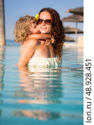 Child kissing smiling woman in swiming pool. Summer vacations concept. Стоковое фото, агентство Ingram Publishing / Фотобанк Лори