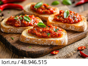 Crusty bread slices are lavishly topped with chunky Ajvar, highlighted by roasted red peppers and eggplant. The vibrant garnish of garlic and chili peppers adds a spicy, rustic charm. Стоковое AI-изображение, AI-художник Nart / Фотобанк Лори