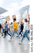 Diverse young adults marching in urban protest with signs. Стоковое AI-изображение, AI-художник Мария Фадеева / Фотобанк Лори