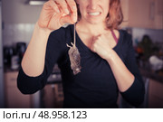 A disgusted young woman is holding a dead mouse by it’s tail in the kitchen. Стоковое фото, агентство Ingram Publishing / Фотобанк Лори