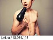 Athletic young man is holding a hair dryer and messing around with it. Стоковое фото, агентство Ingram Publishing / Фотобанк Лори