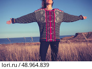 Woman with her arms raised in a field by the sea at sunset. Стоковое фото, агентство Ingram Publishing / Фотобанк Лори
