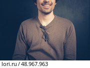 A happy young man is sitting against a black background with a pair of glasses hanging from his collar. Стоковое фото, агентство Ingram Publishing / Фотобанк Лори