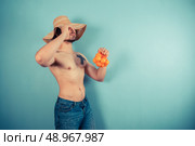 A young shirtless man wearing a large beach hat is holding a net of clementines. Стоковое фото, агентство Ingram Publishing / Фотобанк Лори