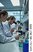 A pharmaceutical lab, scientists in lab coats analyzing samples under microscopes, with shelves of glass vials and sterile white laboratory outfits. Стоковое AI-видео, аниматор Sergey Grishin / Фотобанк Лори