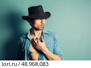 A sexy young cowboy is standing by a blue wall with his shirt unbuttoned. Стоковое фото, агентство Ingram Publishing / Фотобанк Лори