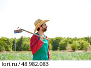 Farmer man with hoe looking at his orchard field with hat. Стоковое фото, агентство Ingram Publishing / Фотобанк Лори