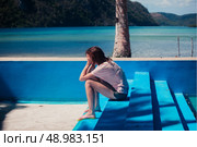 A sad young woman with her head in her hands is sitting in an empty swimming pool by the beach. Стоковое фото, агентство Ingram Publishing / Фотобанк Лори