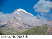The majestic Mount Kazbeg in the clouds against the blue sky. Natural attraction of Georgia. Стоковое фото, фотограф Лазаренко Светлана / Фотобанк Лори