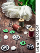 armful white tulip and buttons for clothing on deprecated wooden background.the image is tinted in vintage style. thread and buttons. Стоковое фото, агентство Ingram Publishing / Фотобанк Лори