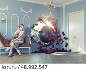wrecking ball enters the room, scaring the woman on the sofa. Photo combination creative concept. Стоковое фото, агентство Ingram Publishing / Фотобанк Лори